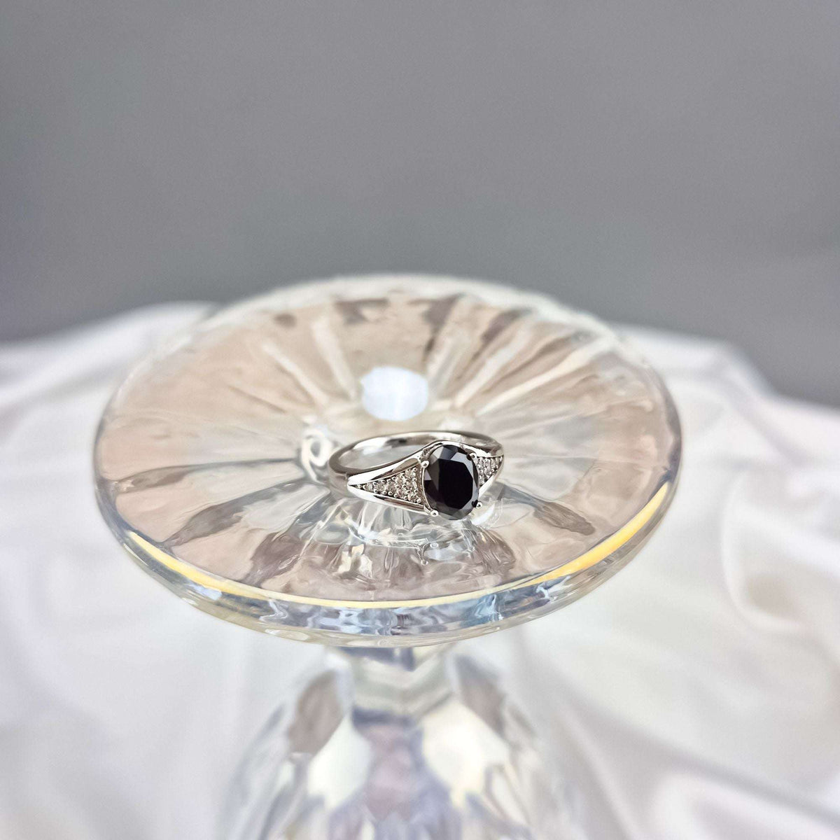 Musta kiviga sõrmus tsirkooniribadega, jäädvustatud kristallalusel ülaltvaates